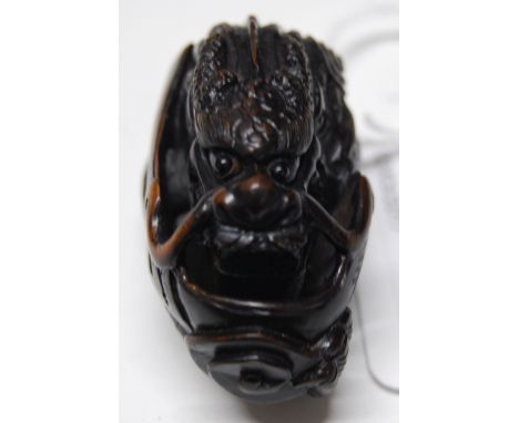 A 20thC carved wood Japanese netsuke, a superbly detailed study of a mythical scaled dragon, coiled and doubled over clinging