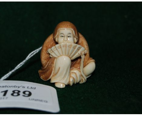 Early 20thC Japanese carved ivory netsuke, a study of a Buddha seated wearing a hooded robe and holding an open fan pressed t