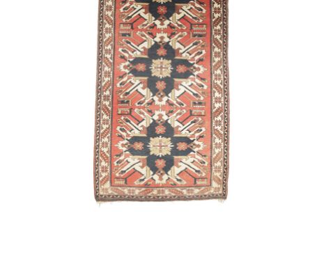 NORTH WEST PERSIAN CARPET of Kazak type, the brick red ground central panel worked with three blue and ivory medallions withi