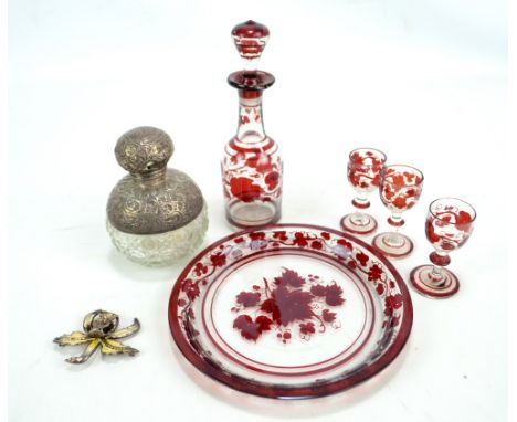 A cut glass silver mounted perfume bottle (badly af), a decorative brooch, and a Bohemian ruby tinted circular glass tray wit
