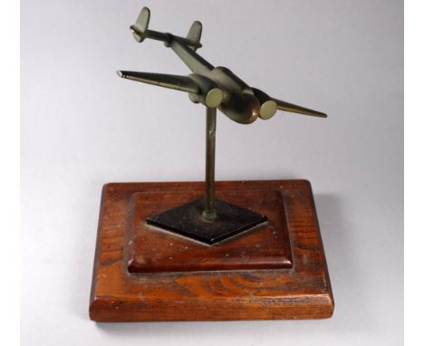 A mid 20th century brass desk stand - modelled as a twin engine aircraft, banking slightly on a stepped wooden base, width 19