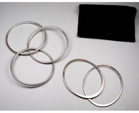A pair of silver bangles of oval form - together with another bangle of three interlinked hoops.