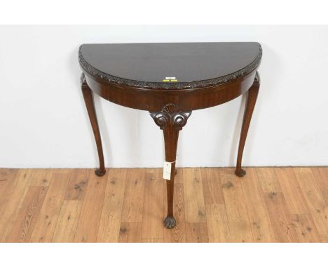 A Georgian style mahogany demi lune card table, the hinged cover with leaf carved edge, opening onto a retractable back leg w