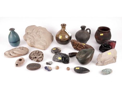 A selection of decorative carved stones, including: a carved sandstone sculpture of three heads, lined up in profile, with ar