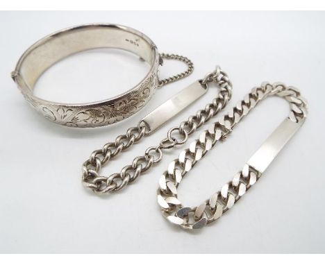 A silver hinged bangle having chased scrolling decoration to one half, with safety chain and two silver identity bracelets, l