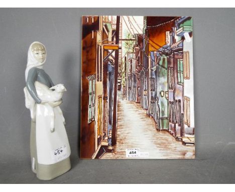 Lot to include a Lladro figurine, Girl With Lamb # 4584, approximately 27 cm (h) and a studio pottery wall tile, depicting a 