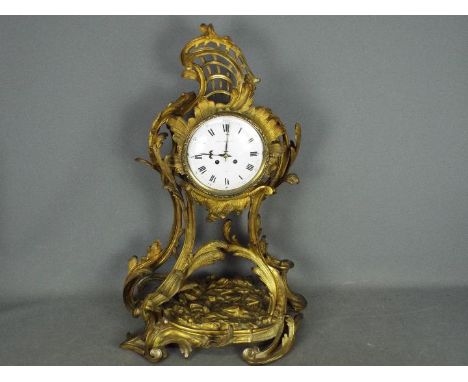 A decorative Rococo or Art Nouveau styled French mantel clock, the case cast in flowing organic forms and gilded, white ename