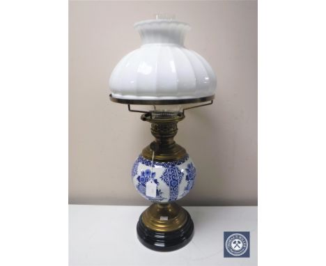 An antique continental brass oil lamp with blue and white china reservoir and white glass shade 