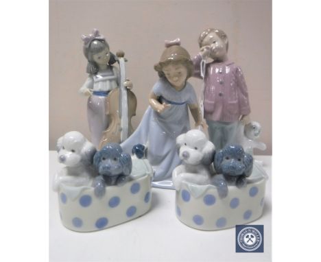 Five Nao figures including boy with teddy bear, girl with puppy, girl with cello and pair of poodle puppies in basket 