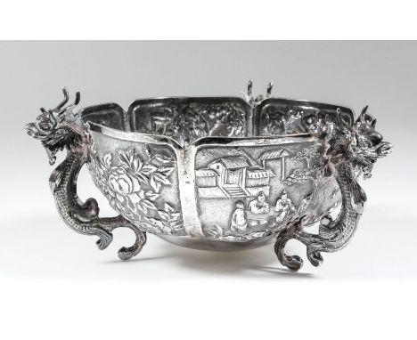 A Chinese silvery metal circular bowl with six panels chased and embossed with dragons, bamboo shoots, blossom and figures in