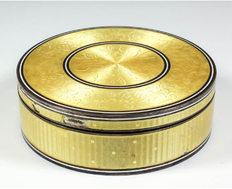 A George V silver and yellow enamel circular box and cover, the lid engraved with leaf scroll and fruiting vines on an engine