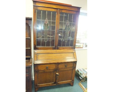 A 1920s oak bureau bookcase with two leaded light coloured glass doors above a fall front, two short drawers and two cupboard