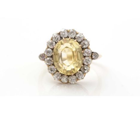 A yellow sapphire and diamond cluster ring, the oval facet cut yellow sapphire measuring 11.9 x 9.8 x 6.6mm, estimated to wei