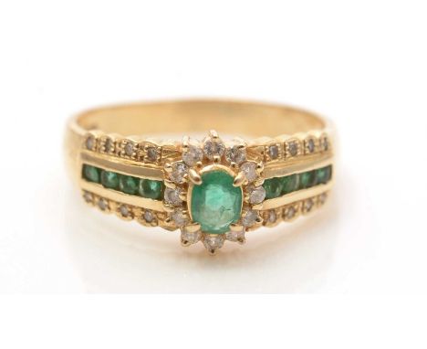 An emerald and diamond ring, the central emerald and diamond cluster flanked by emeralds in channel setting and further diamo