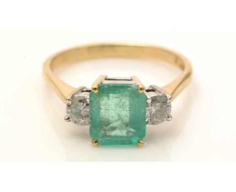 An emerald and diamond ring, the canted rectangular step-cut emerald measuring 9.1 x 7.9 x 4.3mm, flanked by brilliant cut di