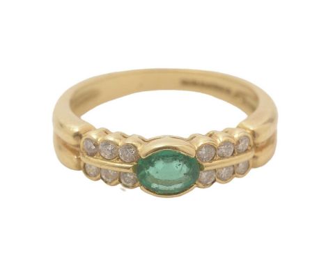 An emerald and diamond ring, the oval facet-cut emerald flanked by twelve brilliant-cut diamonds to shoulders, 18ct yellow go