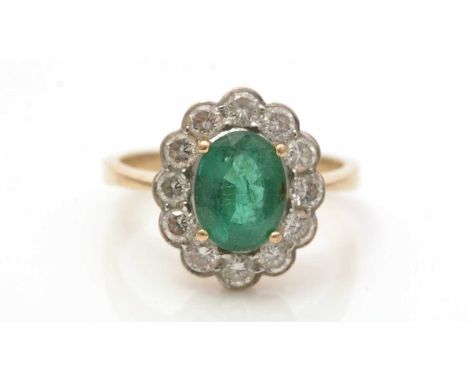 An emerald and diamond cluster ring, the oval facet-cut emerald measuring 9.0 x 6.9 x 4.7mm, surrounded by twelve brilliant c