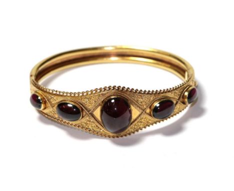 A garnet hinged bangle, five graduated oval cabochon garnets in yellow rubbed over settings to a rope twist detail plaque, to