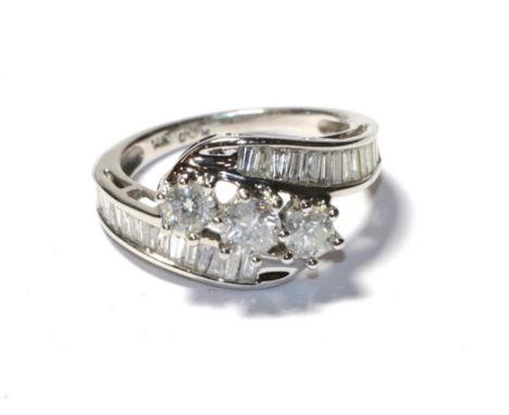 A diamond three stone twist ring, the graduated round brilliant cut diamonds in white claw settings, to tapered baguette cut 