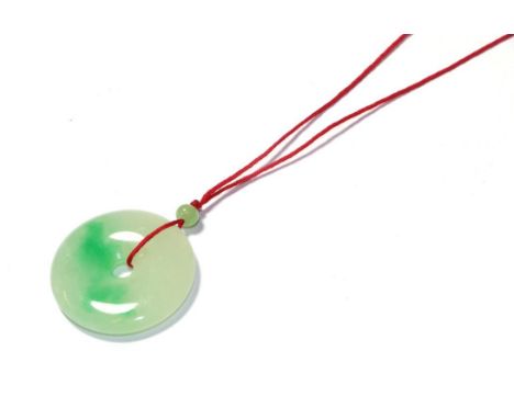 A circular jade pendant, on a red cord necklace, pendant measures 3.7cm diameter .  Gross weight 16.7 grams 