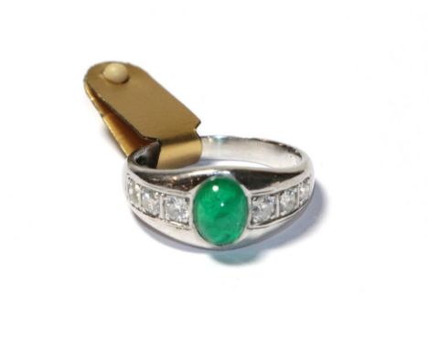 An emerald and diamond ring, the cabochon emerald in a white collet setting, to shoulders inset with trios of round brilliant