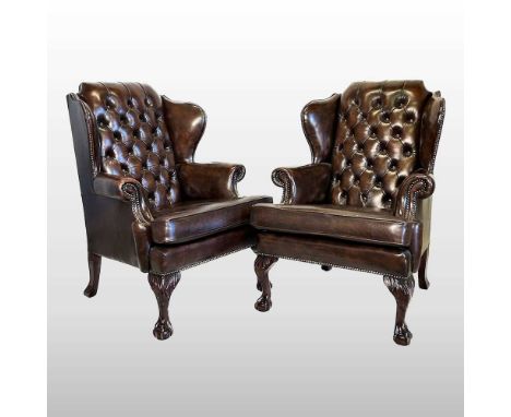 A pair of large brown leather upholstered wing armchairs, 20th century, each with a button back, on cabriole legs, terminatin