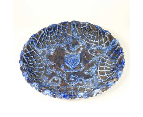 A Castle Hedingham pottery dish, decorated in relief with a blue lattice design on a brown ground, with a heraldic shield to 