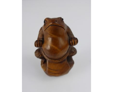 A Japanese Netsuke, in the form of a toad posing as a Tsuma wrestler, character marks to base.