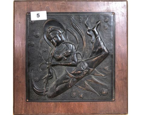 A Himalayan hammered copper panel of a female deity playing a flute and mounted on a wooden panel, overall size 28 x 38cm. Co