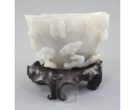 A Chinese greyish-white jade cup or brushwasher, carved in high relief with a chi-dragon, a bat and a lion-dog amid lingzhi f