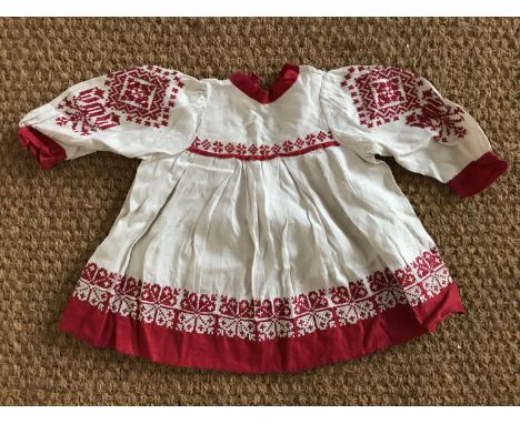 An early 20th Century child's Bohemian influenced cotton dress, of white self-patterned cotton trimmed in red linen, having a