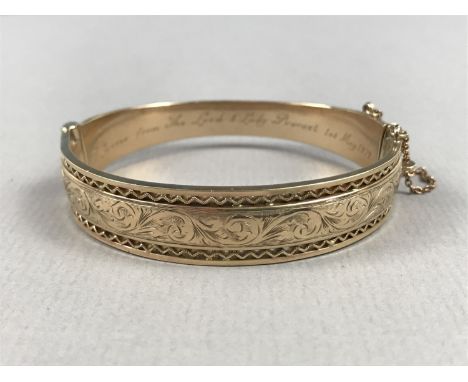 A 9ct gold hinged bangle, the face foliate engraved and edged in an open wirework frame, with engraved inscription to the int