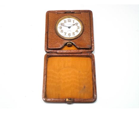 A travelling Clock by Selfridges, with an 8 day movement, enamel dial with luminous Arabic numerals and hands, to a folding l