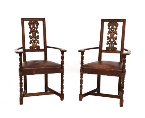 A pair of Arts and Crafts oak armchairs,each with a square back with a central carved foliate relief, with curved armrests, s