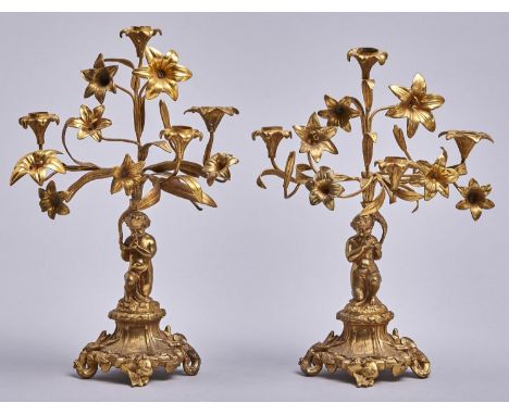 A pair of French fin de siecle gilt brass candelabra, in the form of lilies held aloft by a child, on shaped oval cavetto bas