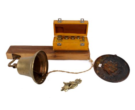 An assortment of four metal items. Including a brass bell, a commemorative wall plaque, a Cornish pixie door knocker and a ca
