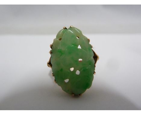 A jade and yellow metal ring, the oval plaque carved with flowers and leaves, claw set on a bifurcated shank,  ring size K 1/