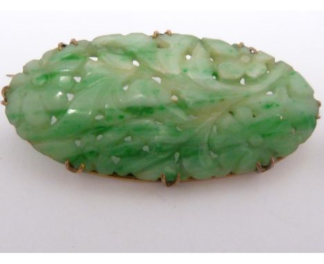 A Chinese Jade Brooch, the green hardstone oval plaque carved with flowers and leaves, set in yellow metal claw mount with pi