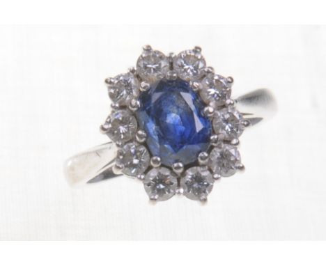 A 18ct white gold sapphire and diamond set cluster ring 
The central oval mixed cut sapphire of approx 7x6mm claw set to a bo