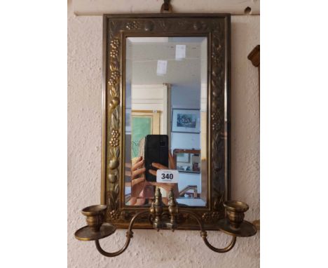 A vintage embossed brass framed bevelled oblong wall mirror with decorative border and twin candle sconces under