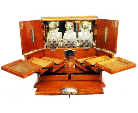 A late 19th Century oak tantalus with silver plated fittings, mirror backed compartment containing three hobnail cut spirit d