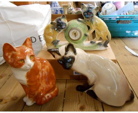 A box containing three pottery cat figurines comprising a Winstanley standing ginger, a Seneshall Siamese and a Jema Holland 