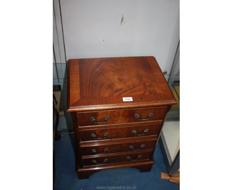 A reproduction Mahogany finished miniature chest of four long drawers having metal handles and standing on bracket feet, 17 1