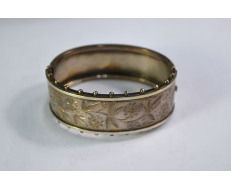 A Victorian silver hinged bangle, half engraved with leaves and flowers, having bead edge