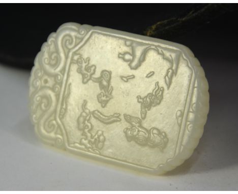 A green jade pendant of whitish hue, decorated with a boy on the obverse and a four-line inscription on the reverse; 5.5 cm l