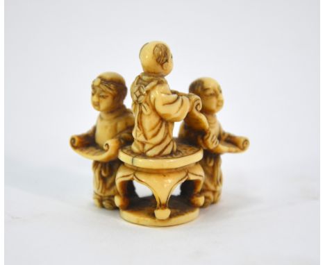 An ivory netsuke of three karako, standing beside one another and studying two makemono, unsigned, 4 cm high, Meiji PeriodSom