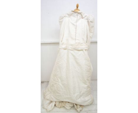 A 1980's wedding dress designed by Gina Fratini, the dress is in raw silk with leg, O Mutton sleeves, a wide pleated sash des