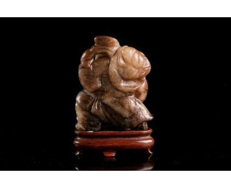 A Chinese carved cream/ khaki green jade figure of a boy with a large peach upon his back. With carved shaped hardwood stand.