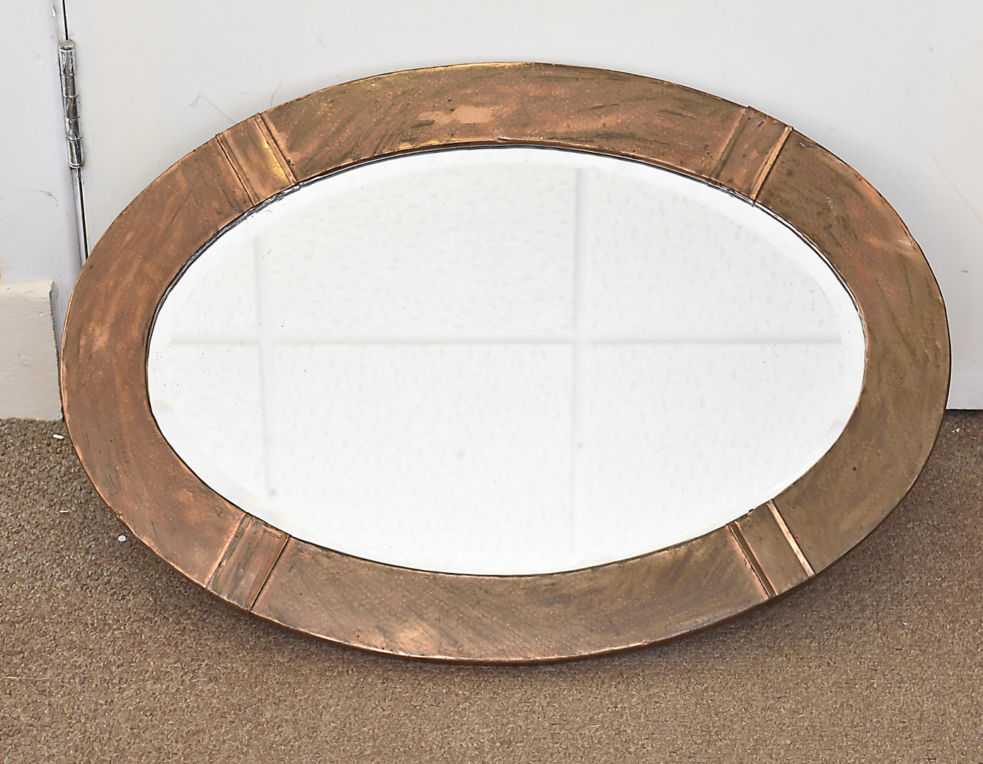 An arts and crafts copper oval framed mirror, with planished decoration