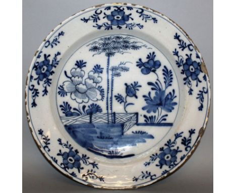 A DELFTWARE CIRCULAR CHARGER, CIRCA 1760, painted with under-glaze blue, fence, trees and flowers, five floral vignettes to t